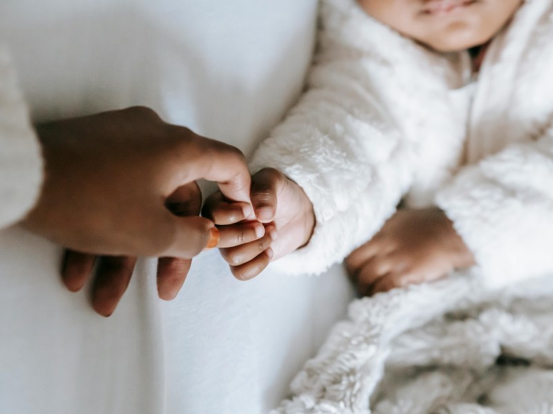 A mother's hand holds a baby's hand against a white backdrop.
